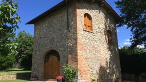 A stone building with a wooden door and arched windows, surrounded by greenery.