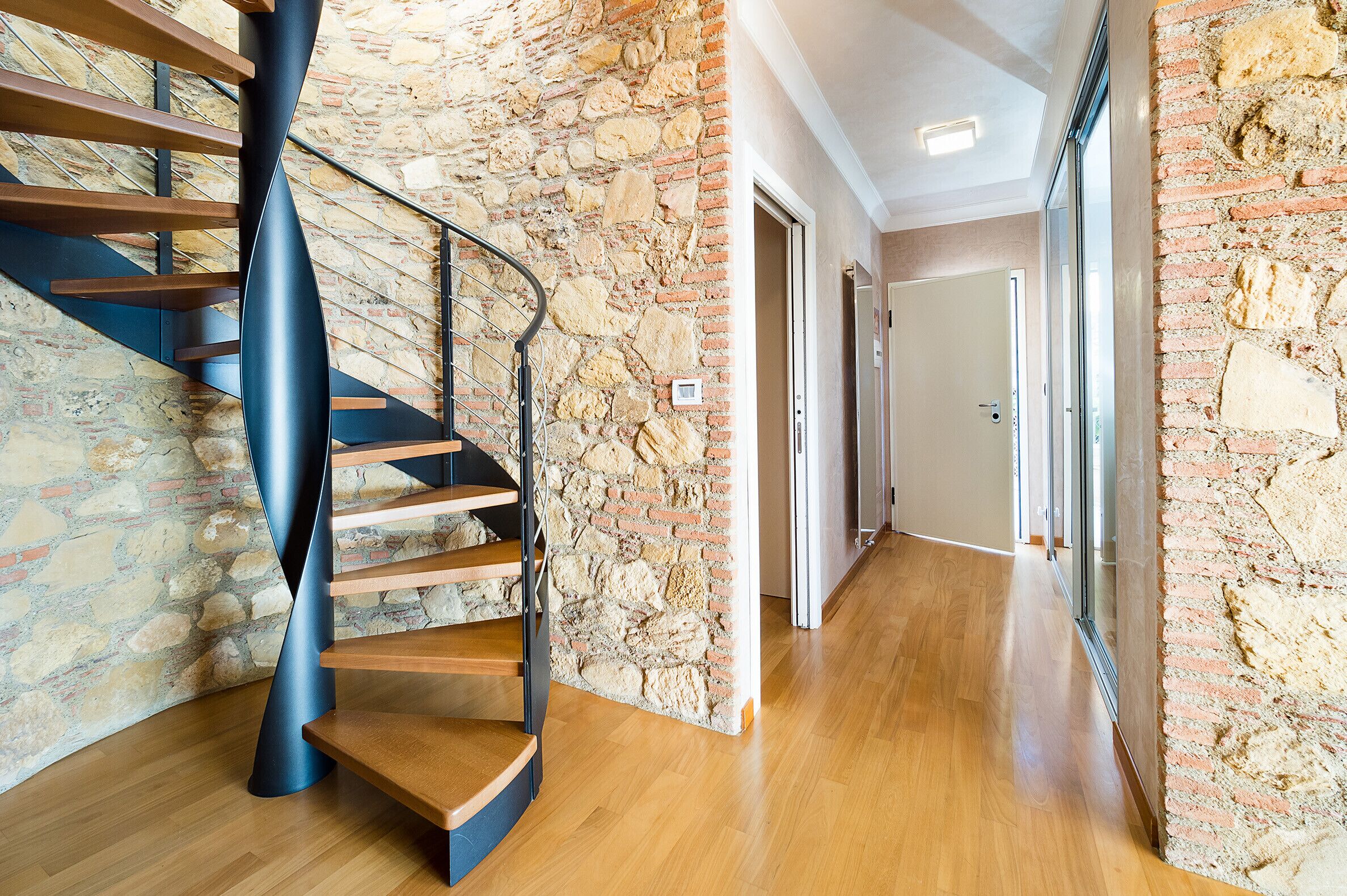 Una escalera moderna con un diseño único, una pared de piedra y un piso de madera.