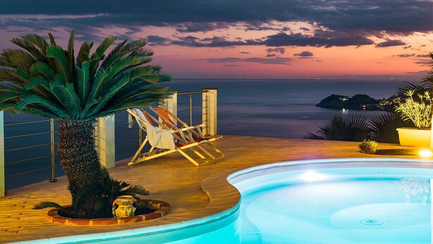A poolside area with a view of the ocean at sunset, a palm tree, and a lounge chair. - Pool villa with sea view near Taormina, Sicily (Taormina)