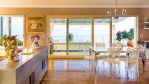 A spacious dining area with a wooden floor, white chairs, and a glass door leading to a balcony with plants. - Pool villa with sea view near Taormina, Sicily (Taormina)