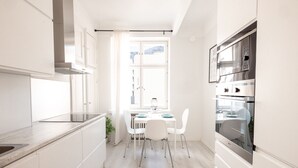 A modern kitchen with white cabinetry, a dining table with chairs, and a large oven. -  2ndhomes Beautiful & Modern 1BR Home with Central Location (Helsinki)