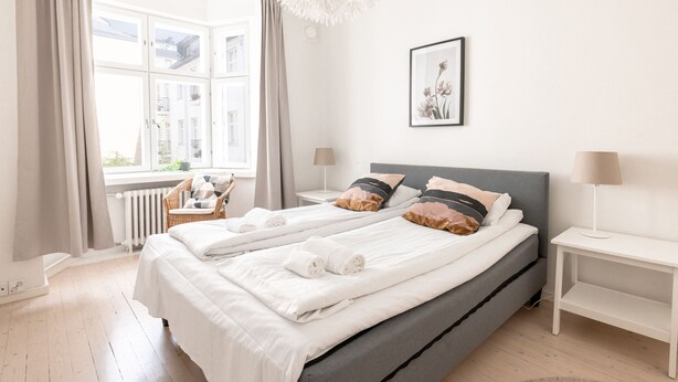 A double bed with white linens, a grey headboard, and two bedside tables with lamps. -  2ndhomes Beautiful & Modern 1BR Home with Central Location (Helsinki)