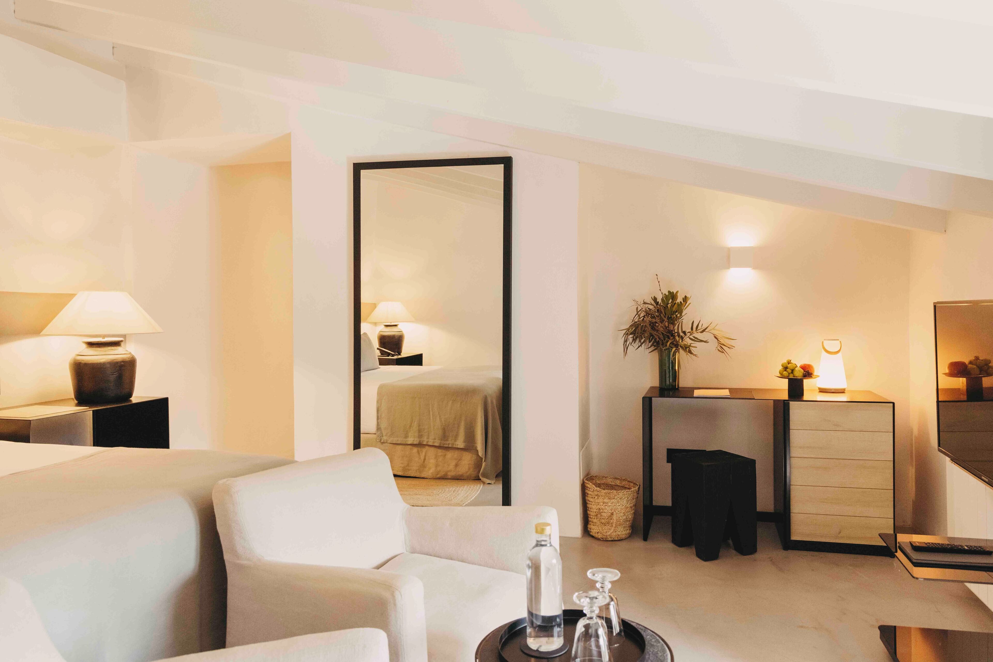 Una habitación de hotel moderna con cama, zona de estar con sofá, escritorio con lámpara y un espejo grande.