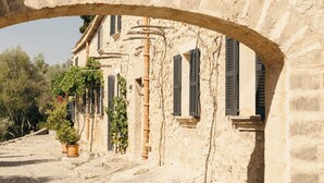 A stone archway with a tiled roof, leading to a building with multiple windows and potted plants. - Finca Serena Mallorca, Small Luxury Hotels (Montuiri)