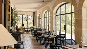 A restaurant with high arched windows, wooden tables, and black chairs. - Finca Serena Mallorca, Small Luxury Hotels (Montuiri)