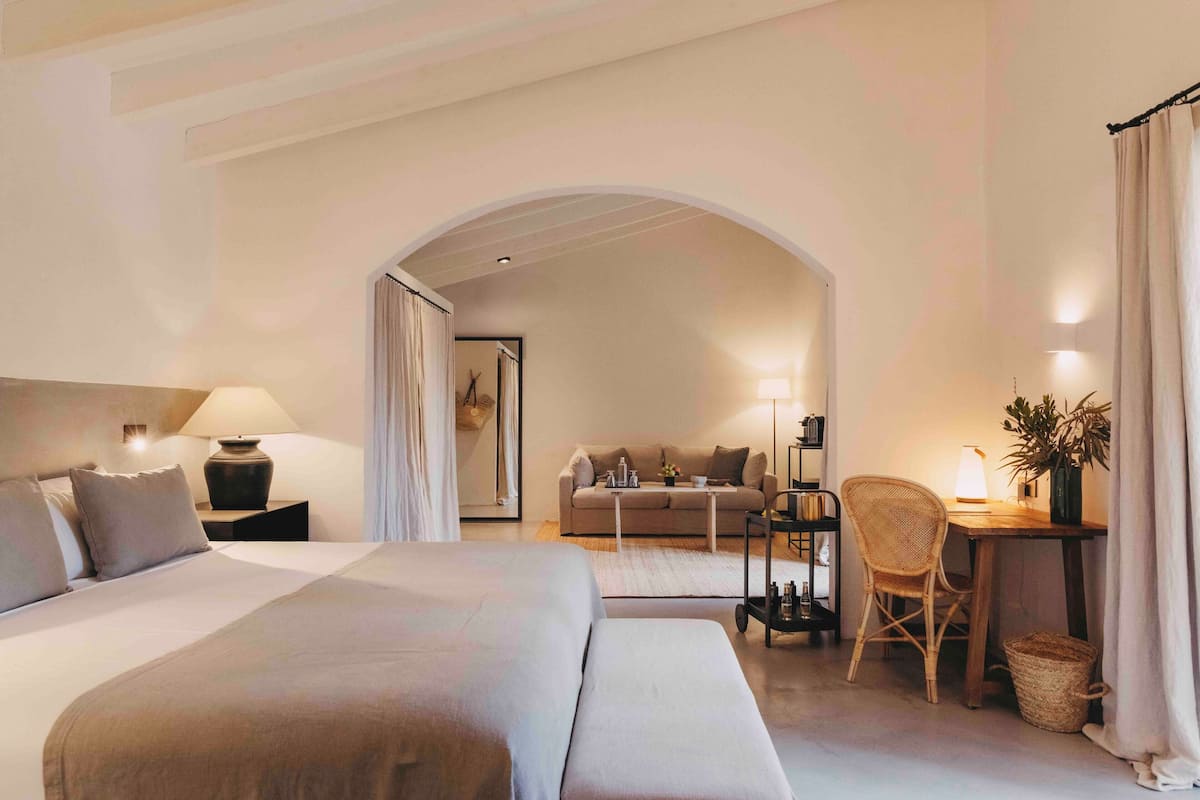Ein Hotelzimmer mit einem großen Bett, einem Schreibtisch mit Stuhl, einem kleinen Tisch und einer Couch im Hintergrund.