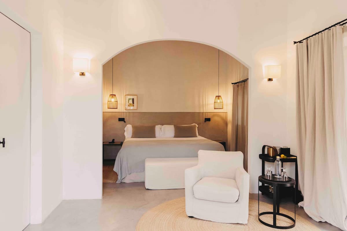 Ein modernes Hotelzimmer mit einem großen Bett, einer Sitzecke mit einem Sessel, einem kleinen Tisch und einem runden Teppich.