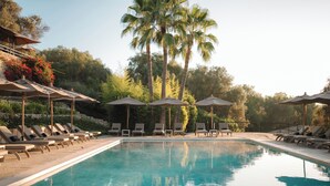 A swimming pool with lounge chairs and umbrellas, surrounded by palm trees and greenery. - Finca Serena Mallorca, Small Luxury Hotels (Montuiri)