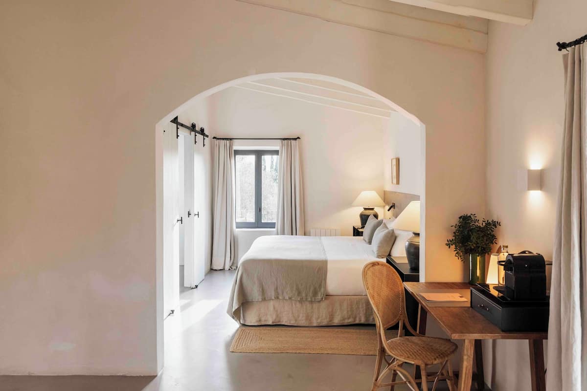 Ein Schlafzimmer mit Bett, Schreibtisch, Stuhl, Lampe und einer Pflanze.
