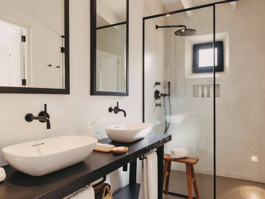 A modern bathroom with a large vessel sink, a dark countertop, a wooden stool, and a glass-enclosed shower area.