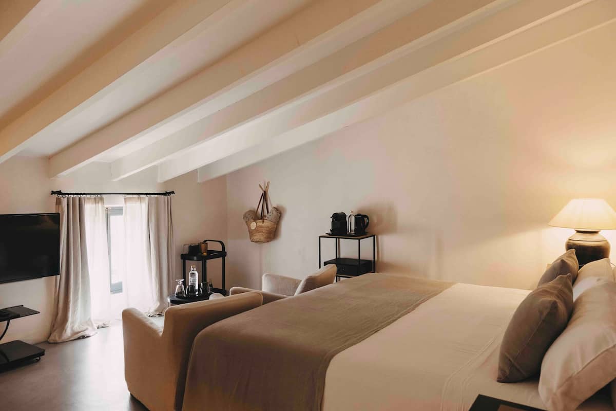 Ein Hotelzimmer mit einem großen Bett, einem Fernseher, einem Schreibtisch und einem Fenster mit Vorhängen.
