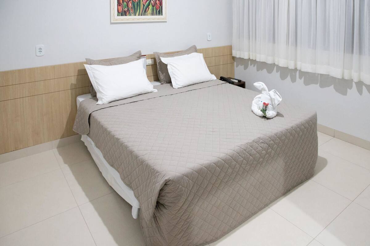 A neatly made bed with a quilted cover, two pillows, and a plush toy on the footboard.