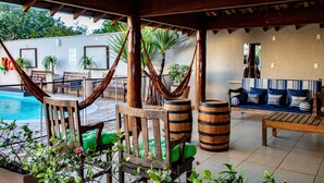 A covered outdoor area with a pool, wooden furniture, and a hammock. - Hotel Jardim (Jardim)