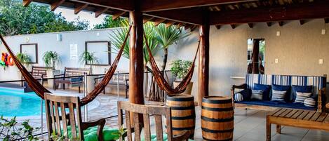 A covered outdoor area with a pool, wooden furniture, and a hammock.