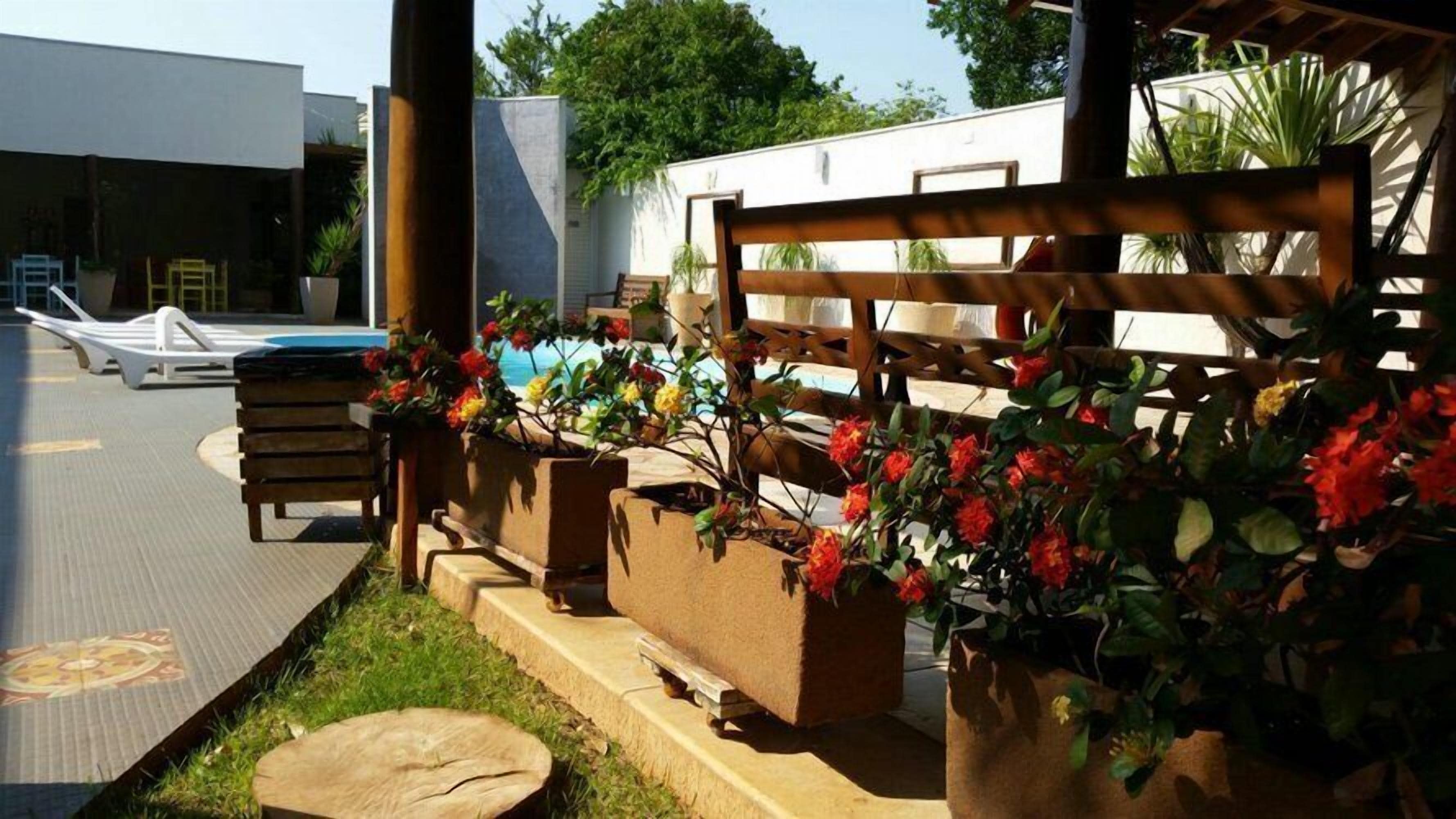 A poolside area with a wooden bench, planters with flowers, and lounge chairs.