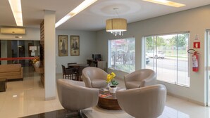 A modern lobby with a reception desk, comfortable seating, large windows, and a fire extinguisher. - Hotel Jardim (Jardim)