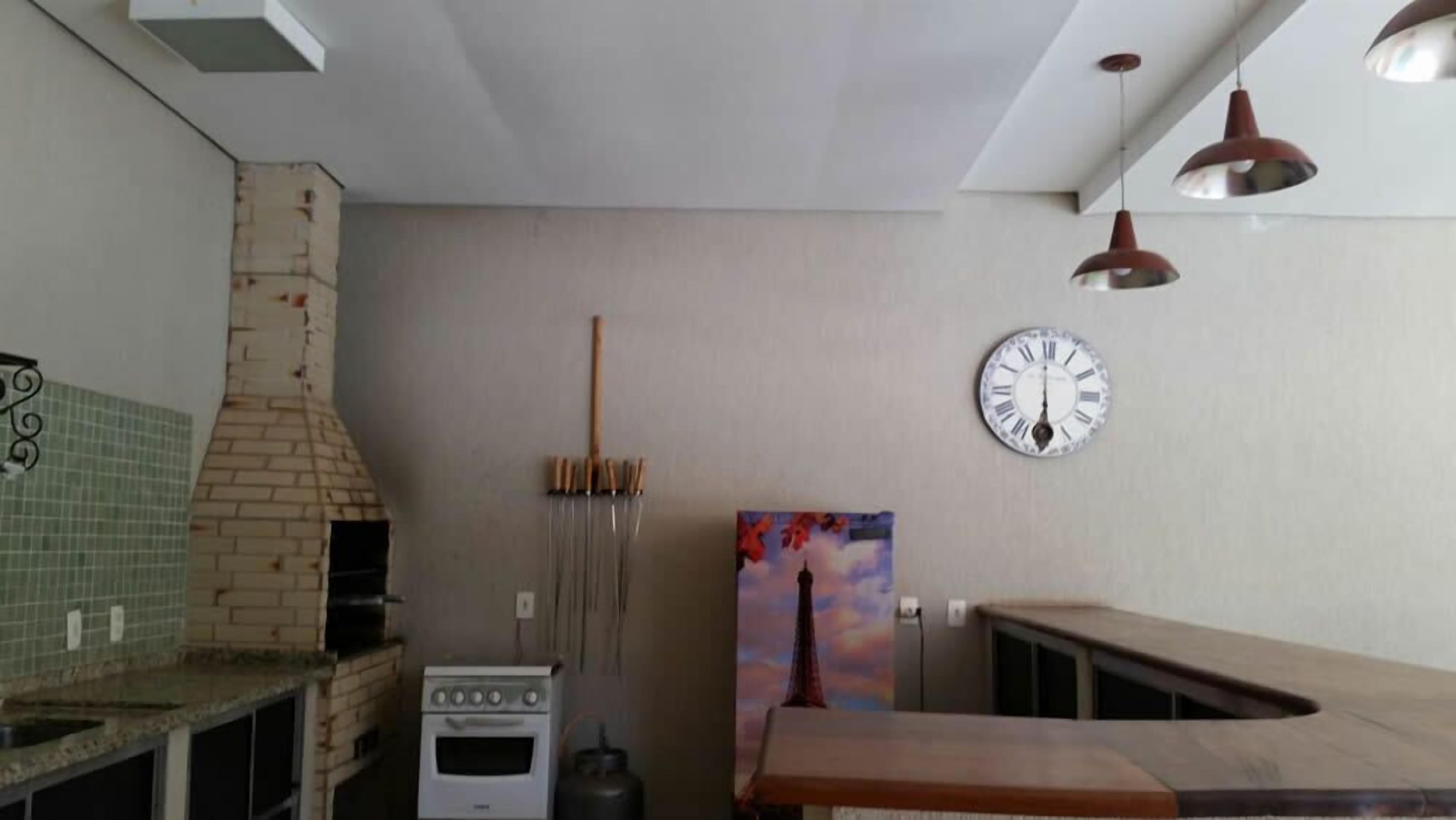 A kitchen with a brick oven, a gas stove, a clock, and pendant lights.