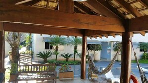 A covered outdoor area with a hammock, a bench, and potted plants. - Hotel Jardim (Jardim)