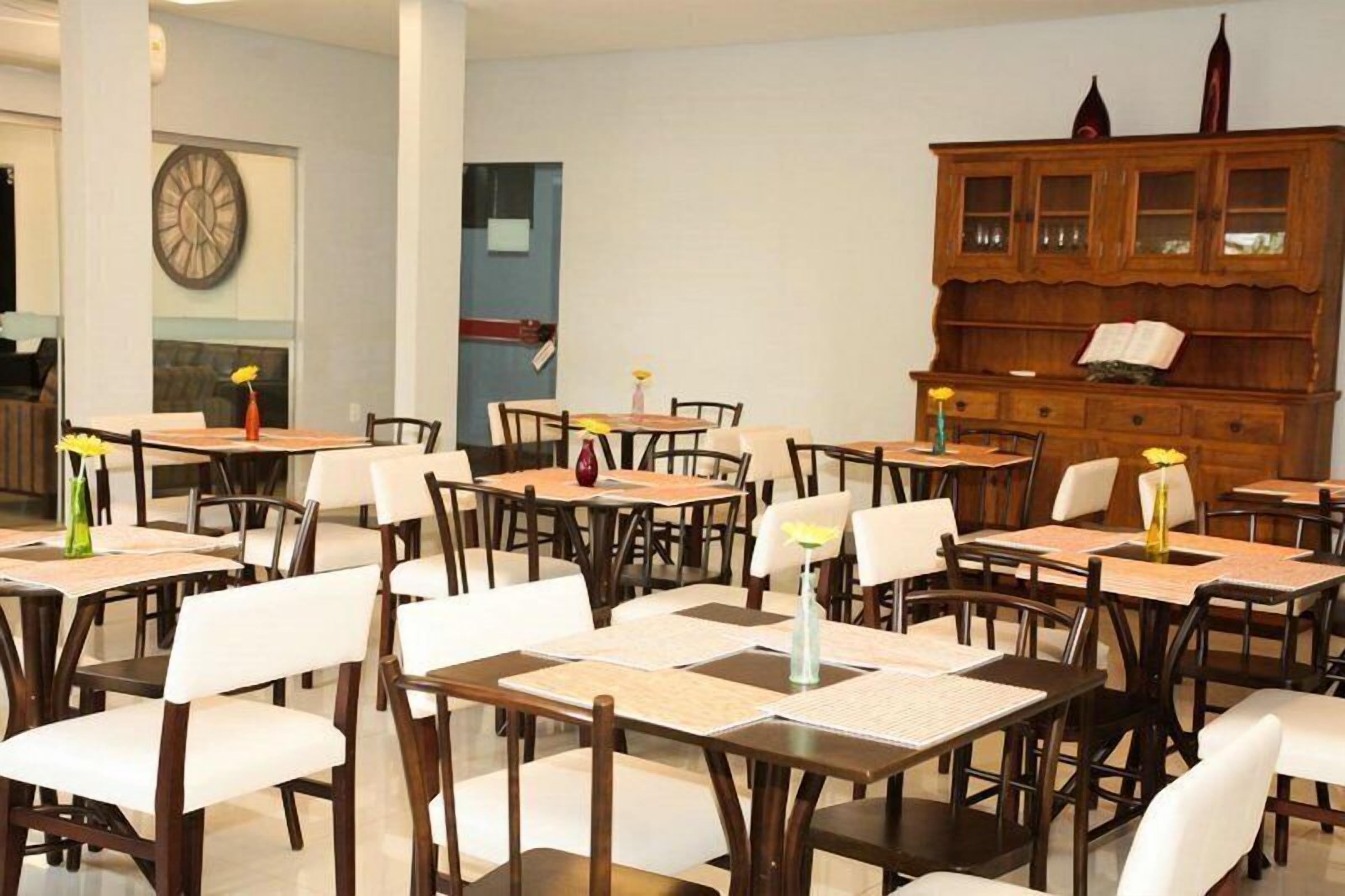 A dining area with multiple tables and chairs, a wooden cabinet with glass doors, and a wall clock.