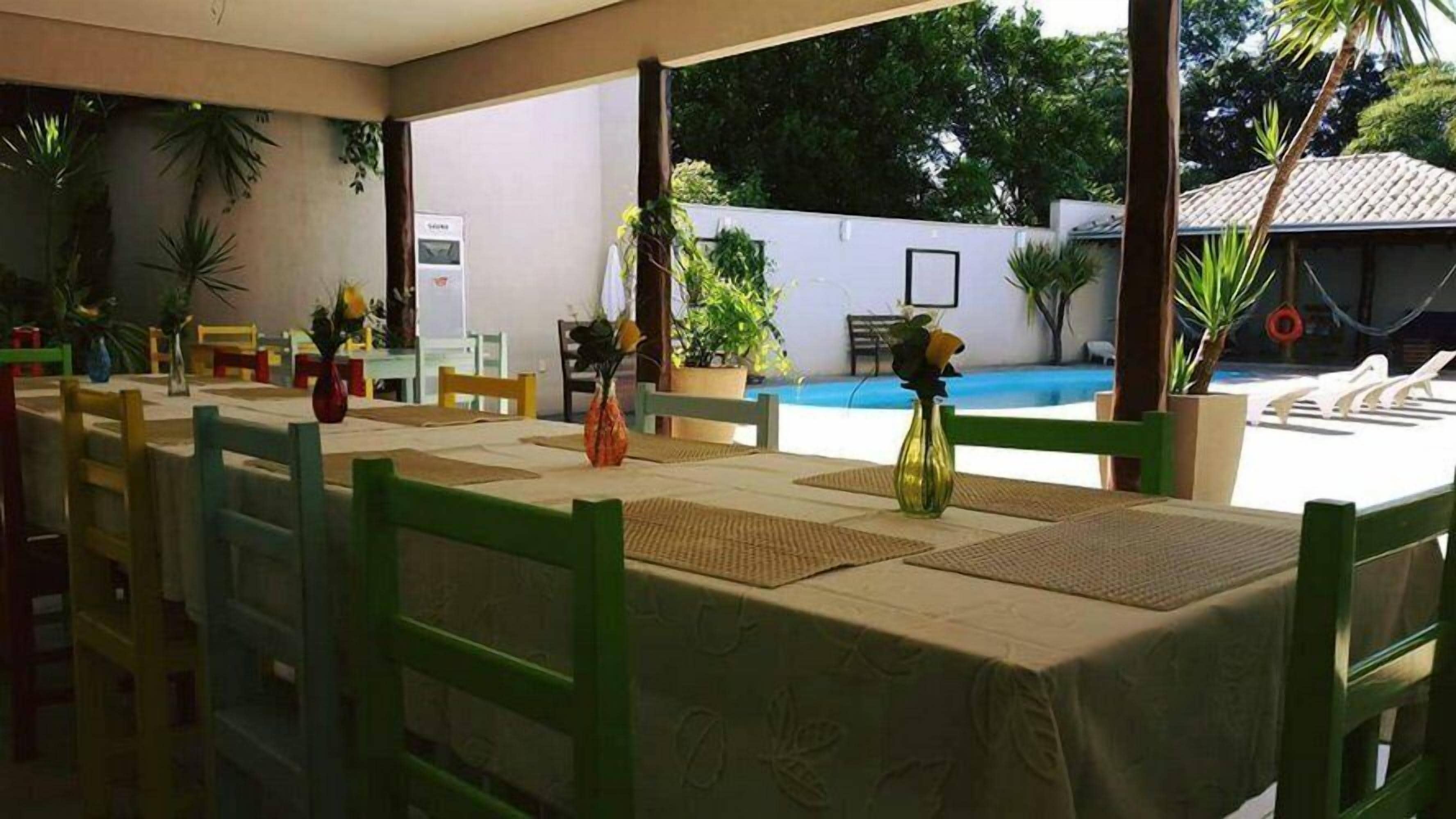 An outdoor dining area with tables and chairs, surrounded by potted plants and a view of a swimming pool.