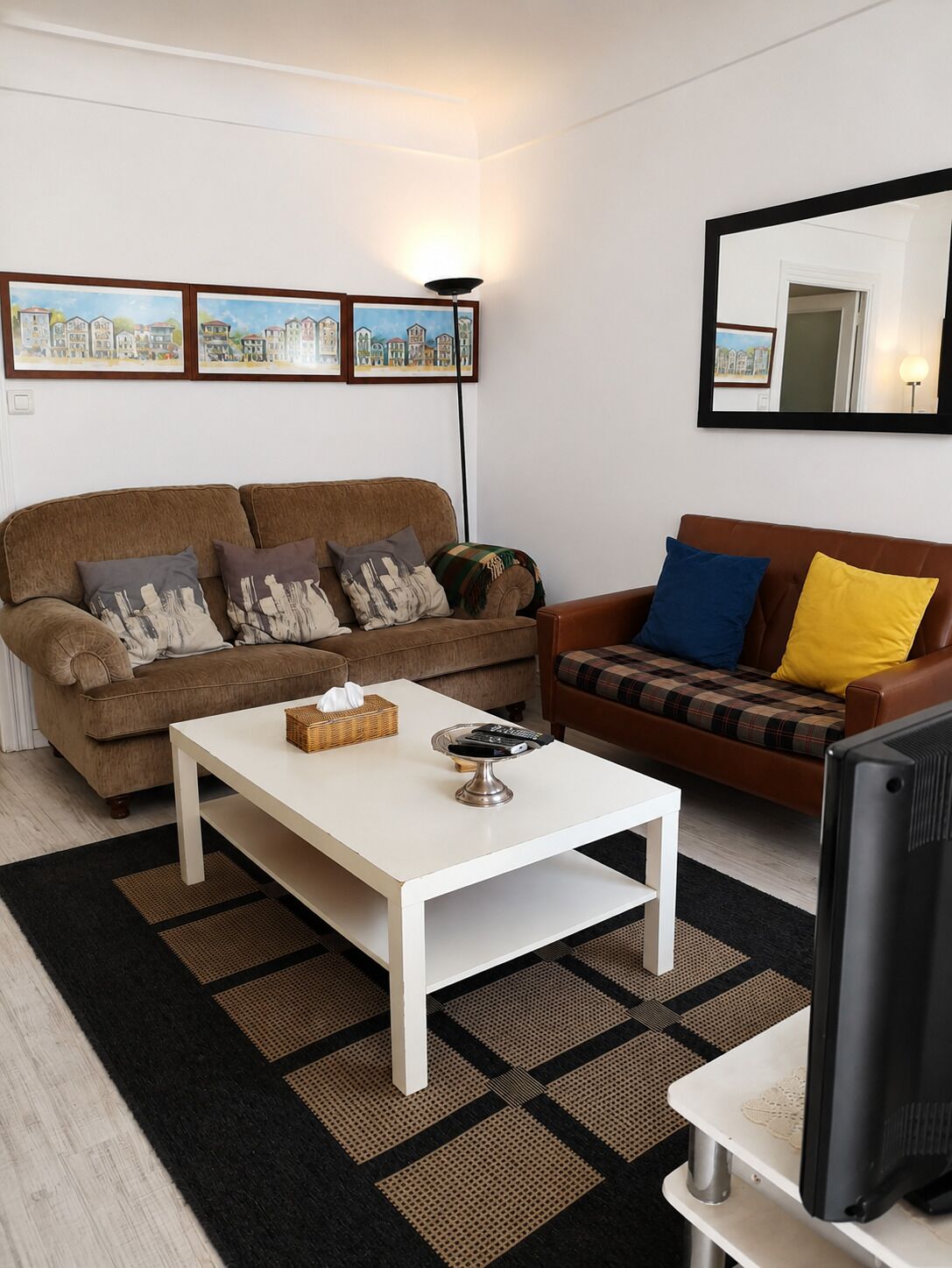 A living room with a brown sofa, a white coffee table, a television on a stand, and a patterned rug.