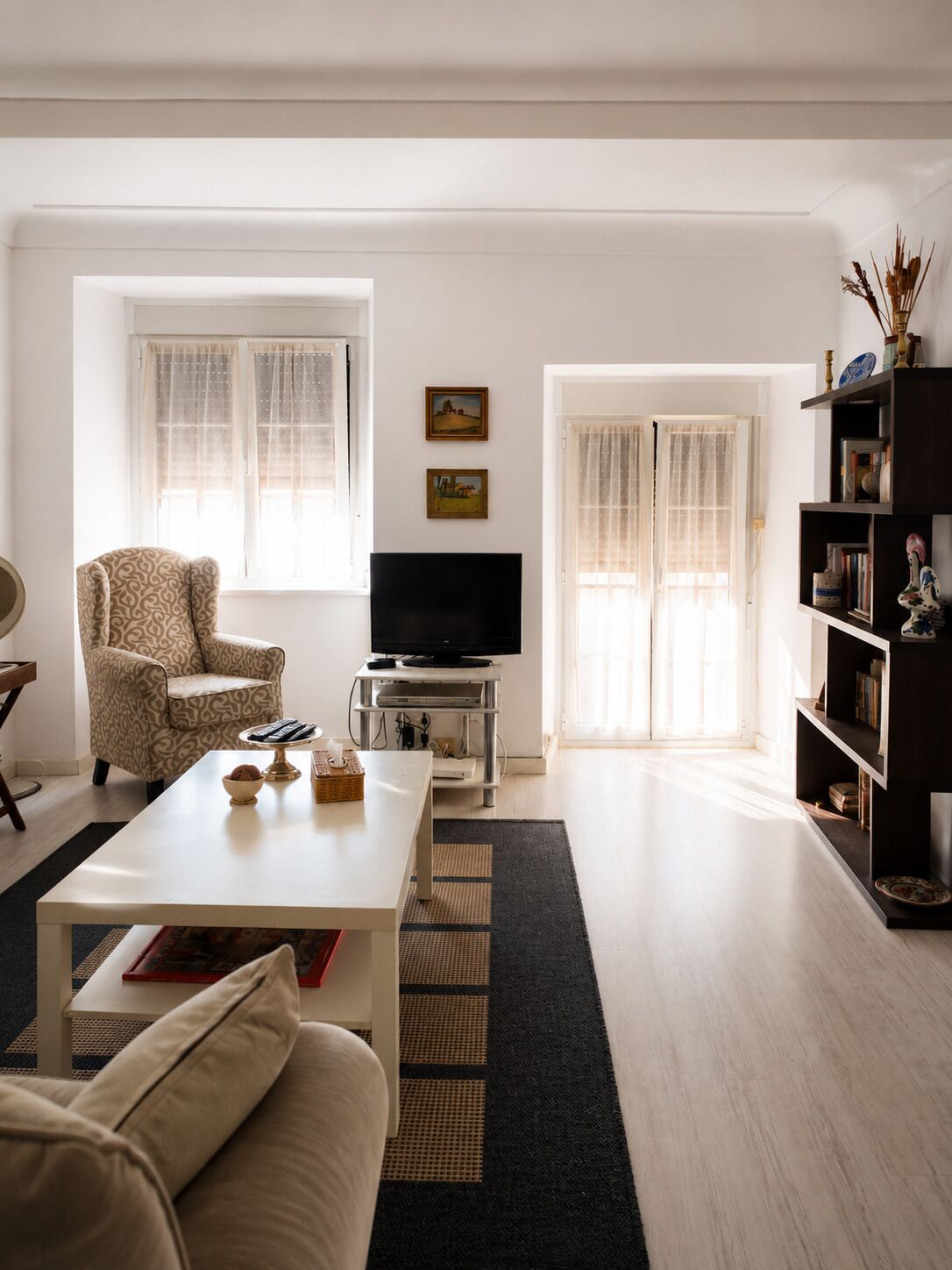 A living room with a sofa, coffee table, TV, patterned armchair, and a bookshelf.