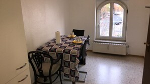 Un pequeño comedor con una mesa dispuesta para dos, una ventana con vistas a coches aparcados y un radiador debajo de la ventana.