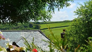 A rural landscape with a stone-roofed building, lush greenery, and a clear sky. - Barley Cottage (Bideford)