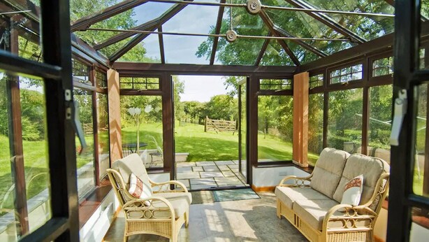 A conservatory with wicker furniture and a view of a grassy area. - Barley Cottage (Bideford)