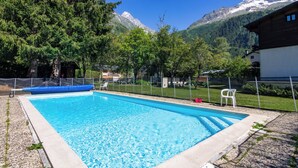 A rectangular swimming pool with clear blue water, surrounded by a fence, trees, and a mountain backdrop. - Résidence le Chardonnet D Studio w/Shared Pool & panoramic views, Argentière (Chamonix), France (Argentière (Chamonix))
