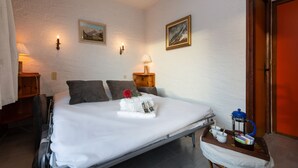 A neatly made bed with pillows, a bedside table with a lamp, a wall-mounted picture, and a door. - Résidence le Chardonnet D Studio w/Shared Pool & panoramic views, Argentière (Chamonix), France (Argentière (Chamonix))