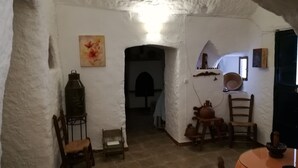 A rustic interior with a stone wall, a wooden chair, a bench, a table with a vase, and a lantern.