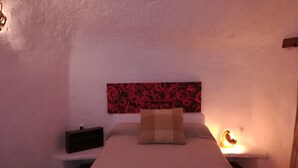 A bedroom with a bed, a nightstand, a wall-mounted lamp, and a red rose-patterned headboard.