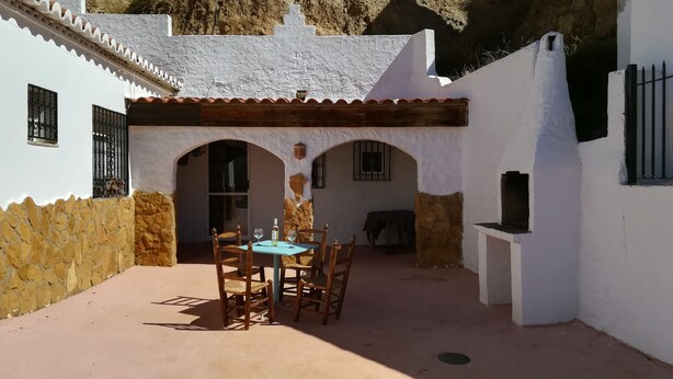 A courtyard with a table and chairs, a stone wall, and a white building with arches.