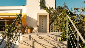 A modern building with a white facade, a door, and a staircase leading up to the entrance.