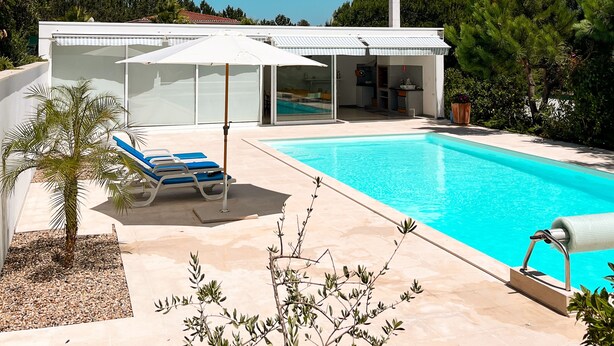 A modern house with a swimming pool, a covered patio, and a view of the surrounding forest.