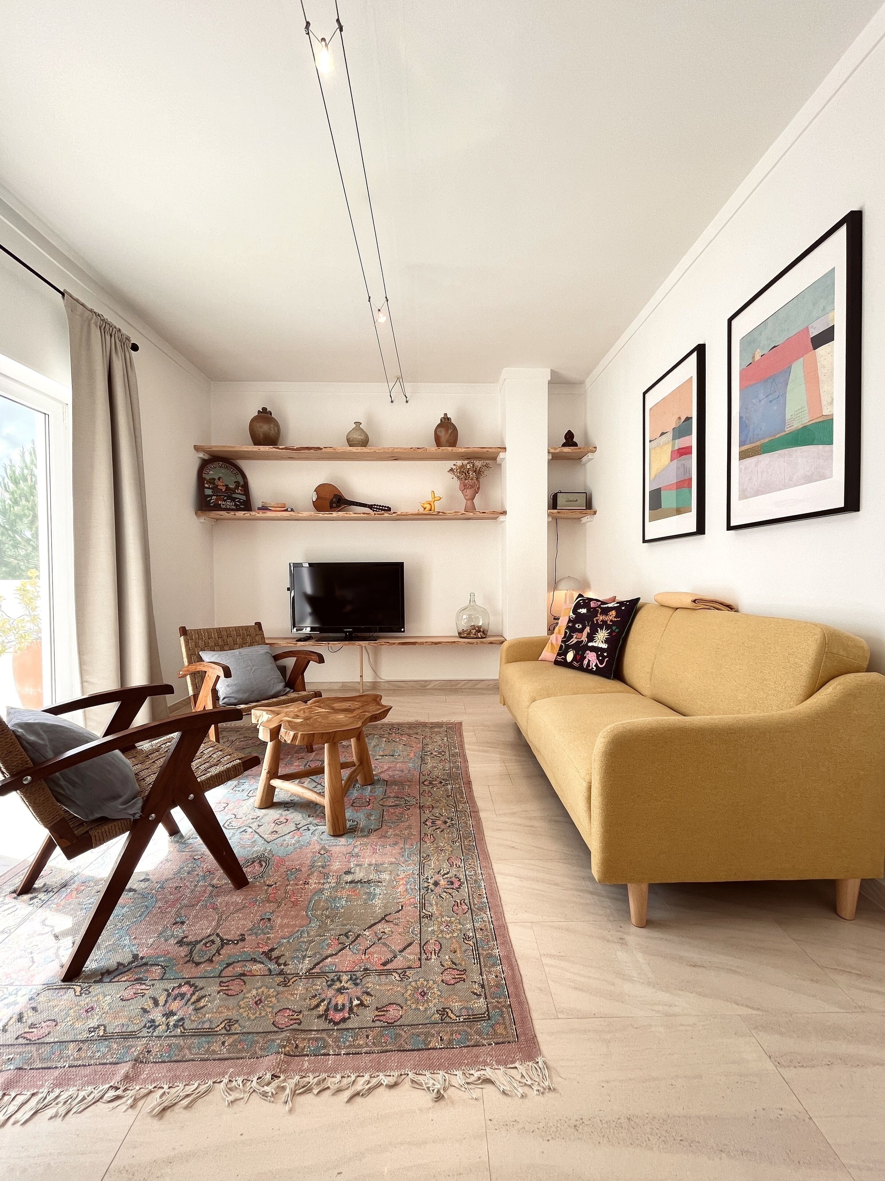 Ein Wohnzimmer mit einer Couch, Sesseln, einem Fernseher, Regalen mit Dekoration und Kunstwerken an der Wand.