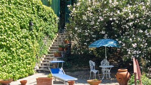 Un espace extérieur ensoleillé, aménagé avec des sièges, comprenant un fauteuil bleu, des chaises blanches et un parasol bleu et blanc à rayures.