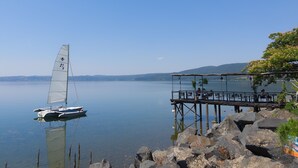 Un voilier sur une eau calme, un quai avec des chaises et des tables, et un ciel dégagé.
