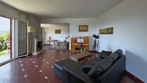 Un salon avec un canapé noir, une table basse en bois et un piano en arrière-plan.