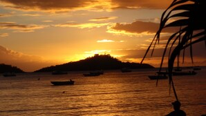 A sunset over a body of water with boats and a silhouette of a person.