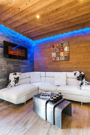 A modern living room with a wooden ceiling, a stone fireplace, a white sectional sofa, and a metal coffee table. - NEW APARTMENT WITH PRIVATE JACUZZI CHEMINEE CLASS 5 STARS (Les Avanchers-Valmorel)