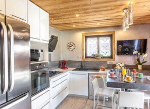 A modern kitchen with stainless steel appliances, white cabinetry, a wooden ceiling, and a dining area with a table and chairs. - NEW APARTMENT WITH PRIVATE JACUZZI CHEMINEE CLASS 5 STARS (Les Avanchers-Valmorel)