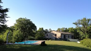A stone house with a swimming pool, surrounded by a grassy yard and trees.