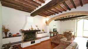 A cozy living room with a fireplace, wooden beams, a sofa, and a dining area.