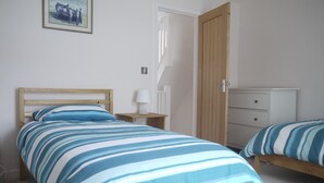Un dormitorio con dos camas, un armario de madera, una mesita de noche con una lámpara y un cuadro enmarcado en la pared.