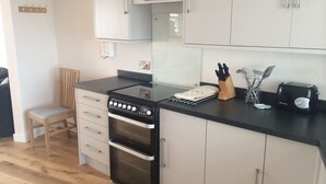 Cocina compacta con estufa, horno y tostadora. Hay una silla y un bloque de cuchillos en la encimera.