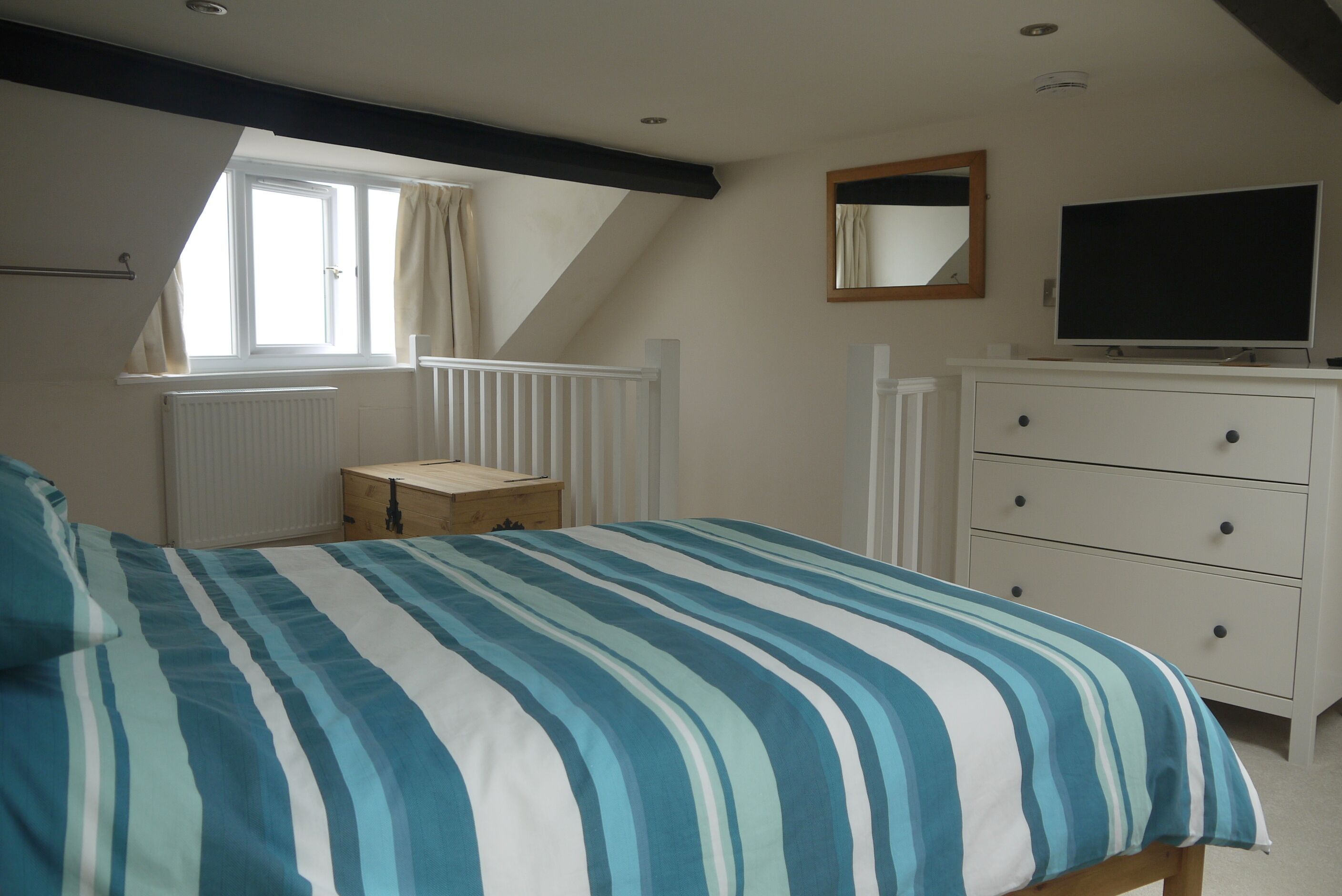 A bedroom with a bed, a dresser, a television, and a window with curtains.