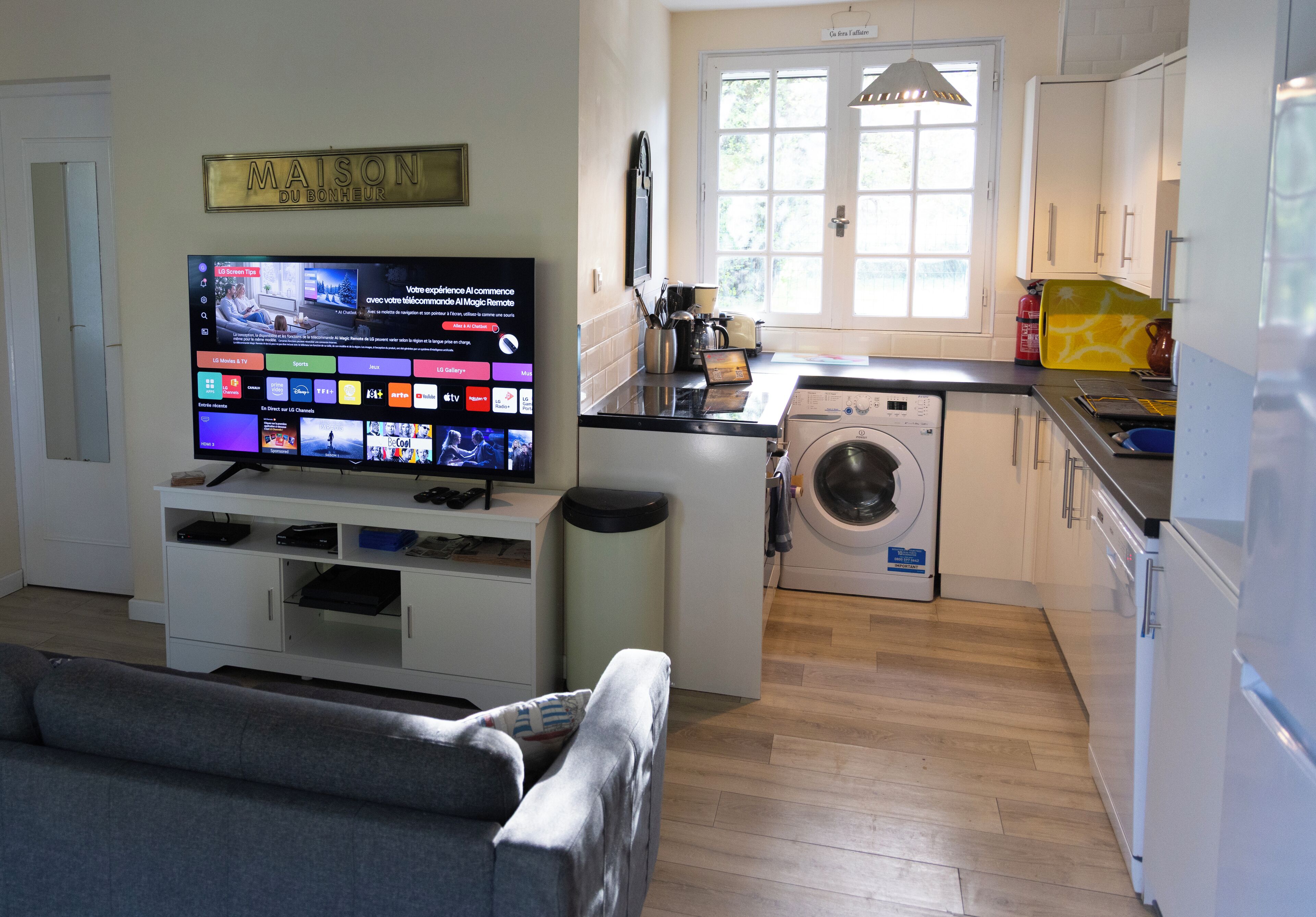 Une cuisine moderne équipée d’un lave-linge, un coin repas avec un canapé et un téléviseur affichant un site web.