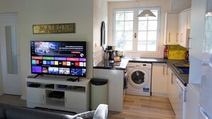 Ett modernt kök med tvättmaskin, en matplats med soffa och en tv som visar en webbplats.